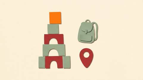 Paper cutout collage of a building-block tower with a bright orange top block, a small backpack, and a map pin on warm cream.
